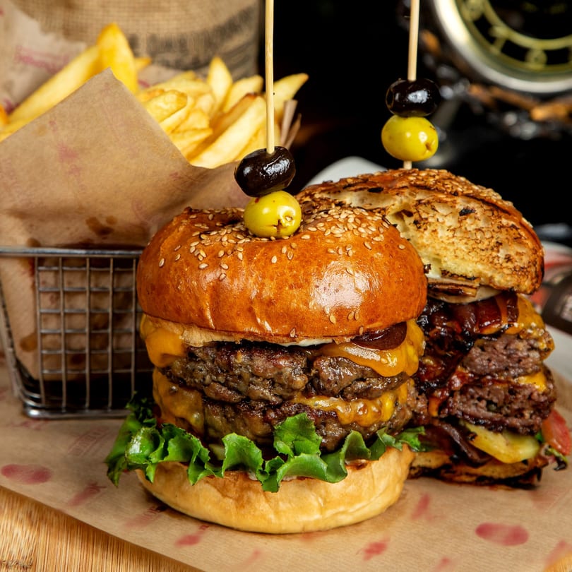 Two double cheeseburgers with lettuce and a side of fries in a metal basket.