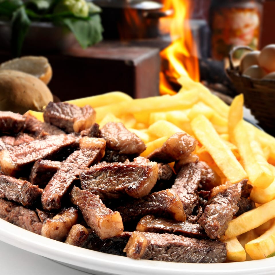 Close-up of steak frites, with crispy fries and sliced steak, against a fiery background.
