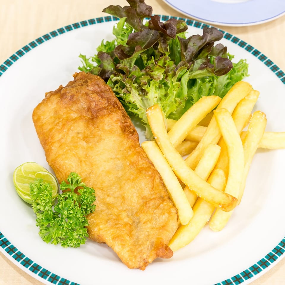 Golden-brown fish and chips with a side salad, lime, and parsley on a white plate.